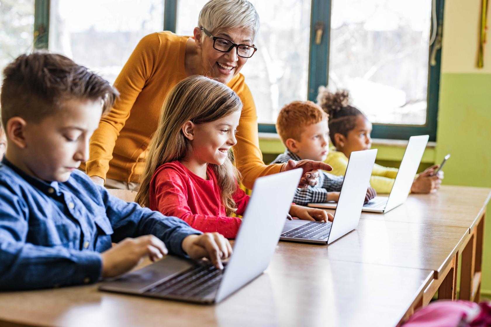 Group of kids on laptops with adult women